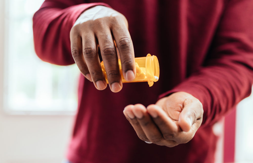 image of african american man in red shirt pouring pills from prescription pill bottle