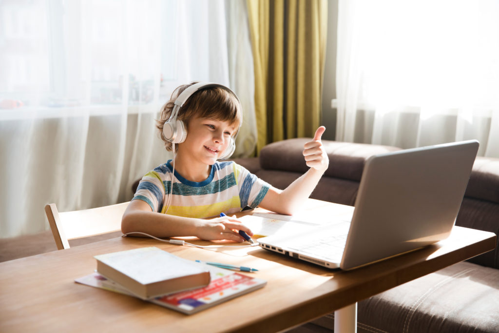 child boy in headphones show sight thumbs up, is using a laptop